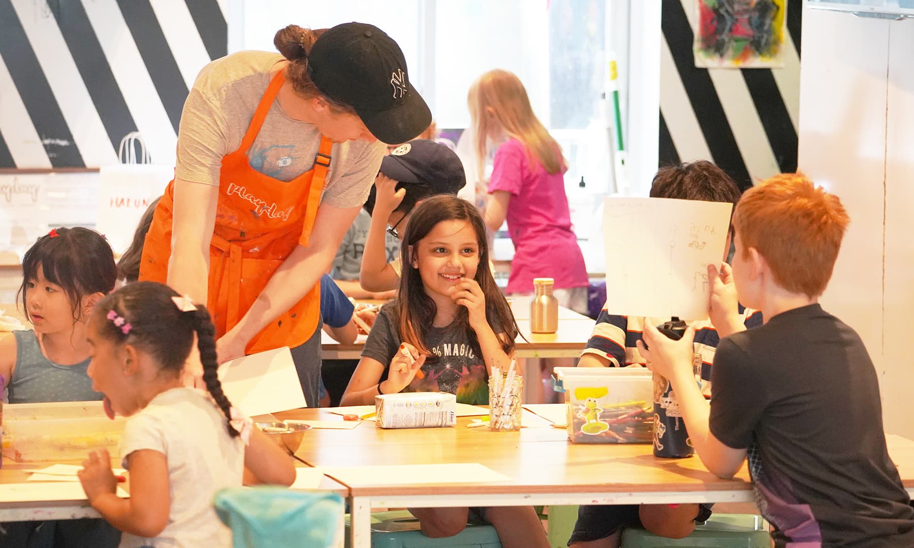 A PLAYDAY teaching artist in the orange apron helping kids at the table